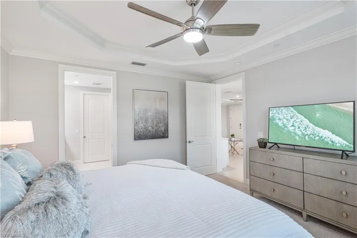 Bedroom featuring light carpet, crown molding, ceiling fan, and a raised ceiling