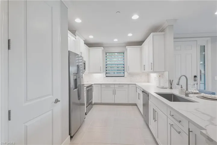 Kitchen with appliances with stainless steel finishes, white cabinets, light stone counters, sink, and tasteful backsplash