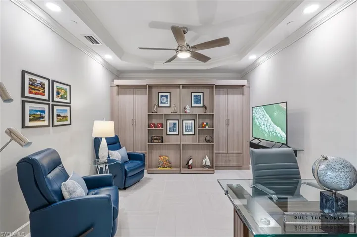 Living area featuring light tile flooring, ceiling fan, a raised ceiling, and crown molding