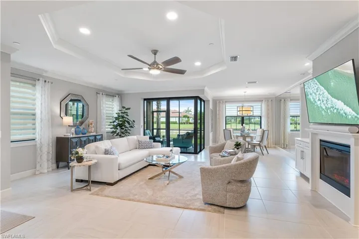 Tiled living room featuring ceiling fan, plenty of natural light, ornamental molding, and a tray ceiling