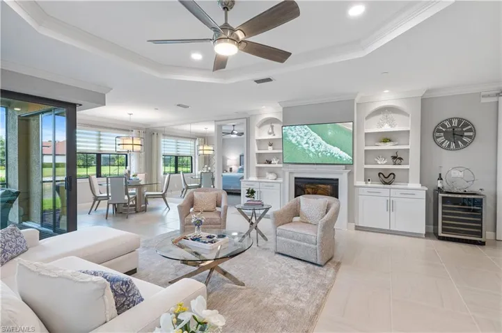 Tiled living room featuring beverage cooler, built in features, a tray ceiling, ceiling fan, and ornamental molding