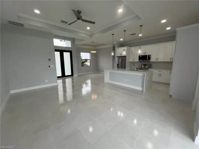 Kitchen with light tile patterned floors, white cabinets, stainless steel appliances, a raised ceiling, and a center island with sink