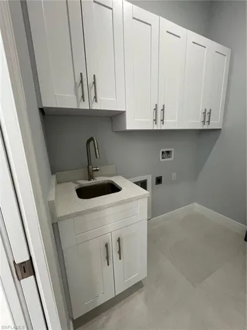 Clothes washing area with sink, electric dryer hookup, cabinets, light tile patterned floors, and washer hookup