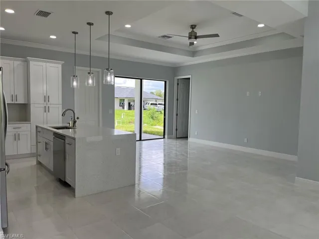 Kitchen with ceiling fan, a tray ceiling, sink, dishwasher, and a kitchen island with sink