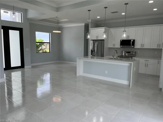 Kitchen featuring white cabinetry, stainless steel appliances, hanging light fixtures, crown molding, and an island with sink