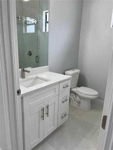 Bathroom with tile patterned floors, toilet, vanity, and an enclosed shower
