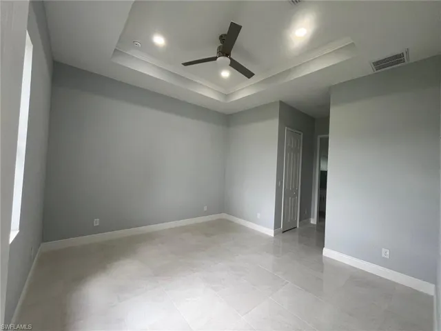 Tiled spare room featuring ceiling fan and a tray ceiling
