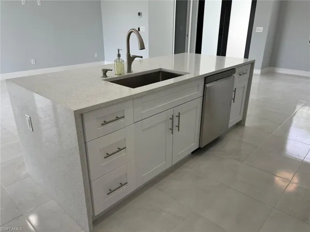 Kitchen featuring light tile patterned flooring, light stone counters, an island with sink, stainless steel dishwasher, and sink