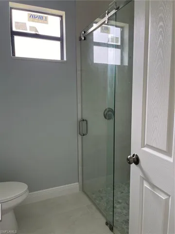 Bathroom with toilet, a shower with door, and tile patterned flooring