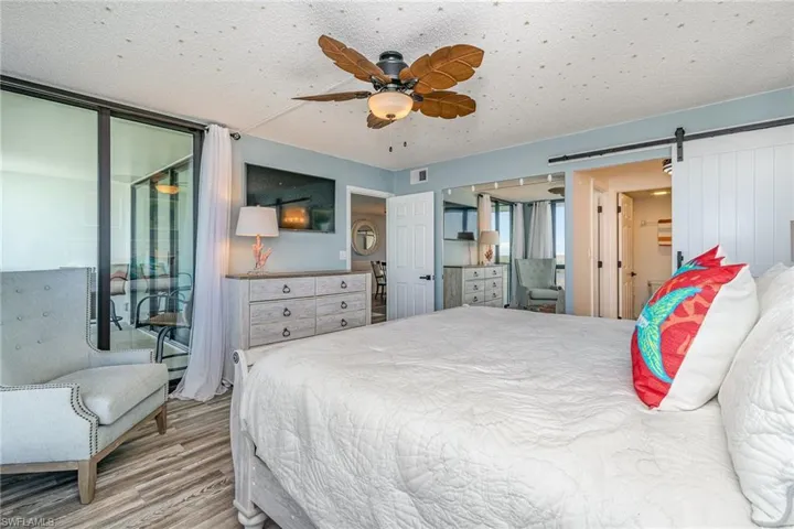 OWNER'S SUITE.  ENTRANCE TO EN-SUITE BATH SHOWN MIDDLE RIGHT.  TRACK BARN DOOR.  CUSTOM LARGE MIRROR.  UPDATED CEILING FAN.