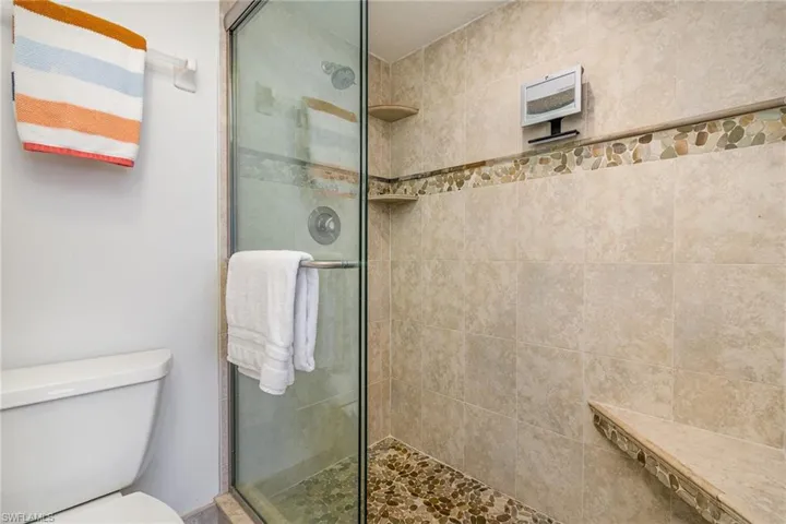OWNER'S SUITE SHOWER.  FULL-HEIGHT TILED WALLS WITH DECORATIVE BORDER.  BUILT-IN SHELVES AND SEAT.  GLASS SLIDING DOORS.