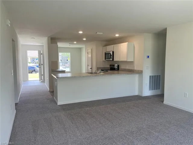 Kitchen featuring dark colored carpet, a peninsula, stainless steel appliances, white cabinetry, and recessed lighting