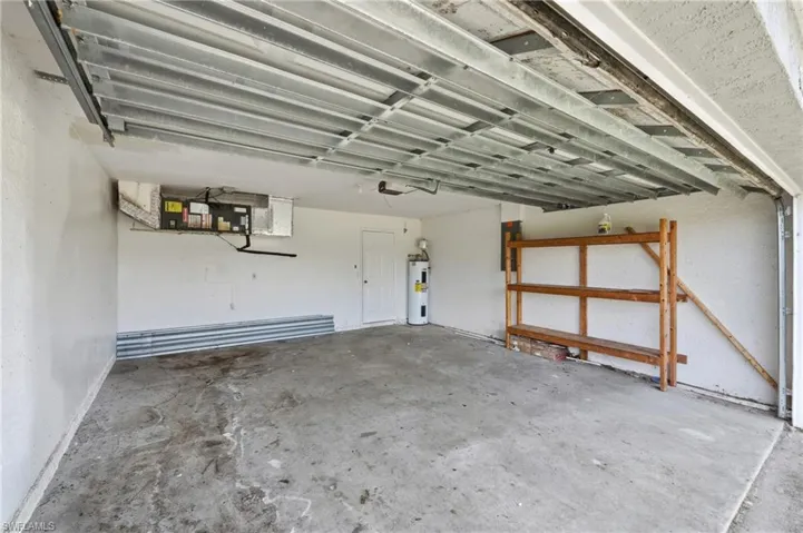 Concrete flooring, white painted walls, water heater, wood shelving, and garage door mechanism