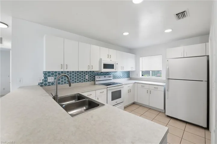 White cabinetry, patterned tile backsplash, stainless steel double basin sink, recessed lighting, and tile flooring