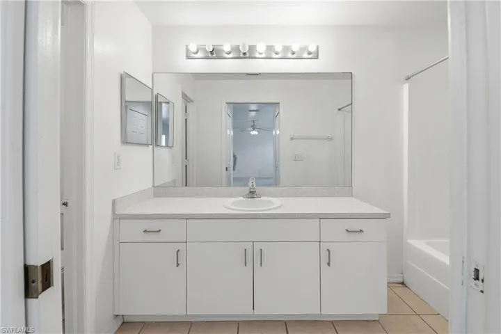 White vanity with integrated sink, expansive mirror, and overhead vanity lighting