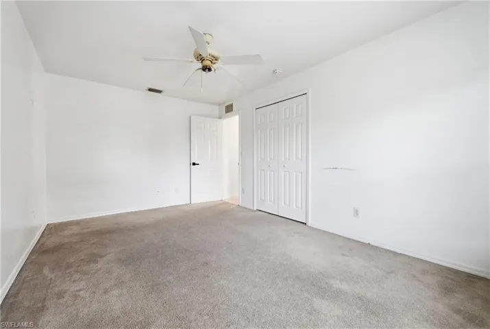 Carpeted room with white walls, a ceiling fan, and bi-fold closet doors