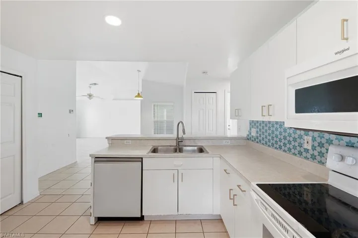 Kitchen featuring white cabinetry, a double basin stainless steel sink, a tile backsplash with a star pattern, a built-in microwave, and a dishwasher