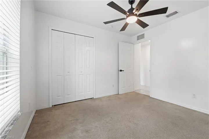 Neutral wall tones, carpeted flooring, window with blinds, bi-fold closet doors, and a ceiling fan with integrated lighting