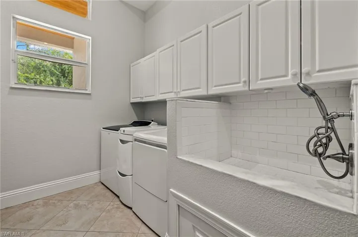 Clothes washing area with cabinets, washer and clothes dryer, and light tile patterned floors
