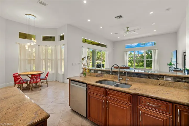 Kitchen with dishwasher, light stone countertops, sink, light tile patterned flooring, and ceiling fan