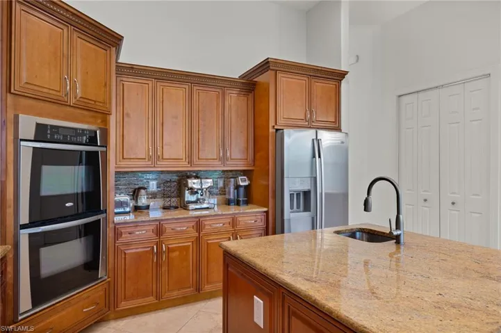 Kitchen with light stone countertops, backsplash, stainless steel appliances, sink, and light tile patterned flooring