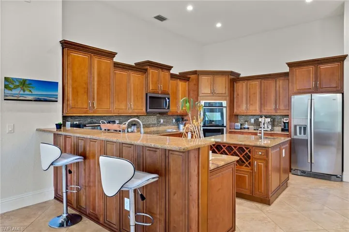 Kitchen with light tile patterned floors, a breakfast bar, stainless steel appliances, kitchen peninsula, and decorative backsplash