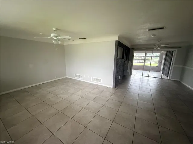 Neutral-tone ceramic tile flooring, ceiling fans with integrated lighting, and a textured brick accent wall, featuring glass sliding doors leading to an enclosed patio