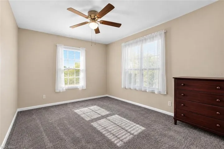 Soft gray carpet flooring, neutral painted walls, white window trim, and a ceiling fan with integrated lighting