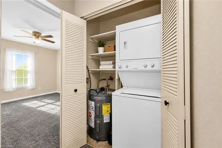 Laundry closet with stacked washer and dryer, built-in shelving, and louvered bifold doors