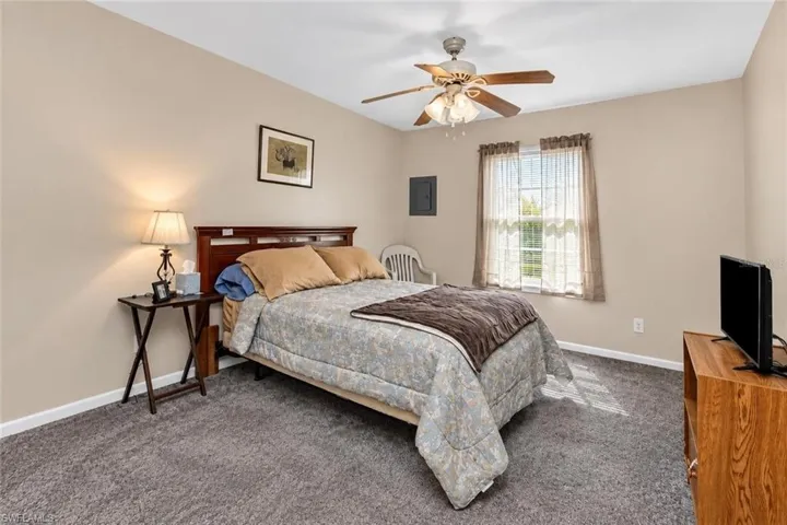 Neutral tone wall paint, textured carpet flooring, ceiling fan with integrated lighting, window with ample natural light, and a wood-finish headboard
