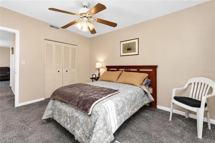 Neutral wall tones, gray carpeting, a ceiling fan with integrated lighting, and louvered bi-fold closet doors