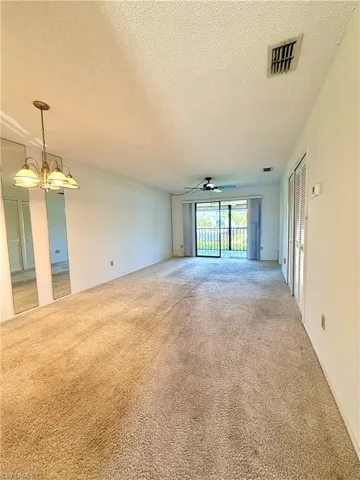 Spare room with light colored carpet, a textured ceiling, a ceiling fan, and suspended lighting