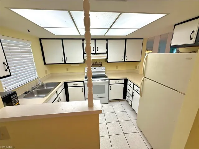 Kitchen featuring white appliances, light countertops, white cabinetry, light tile patterned floors, and a peninsula