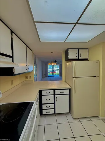 Kitchen featuring electric range oven, freestanding refrigerator, white cabinetry, light countertops, and light tile patterned floors