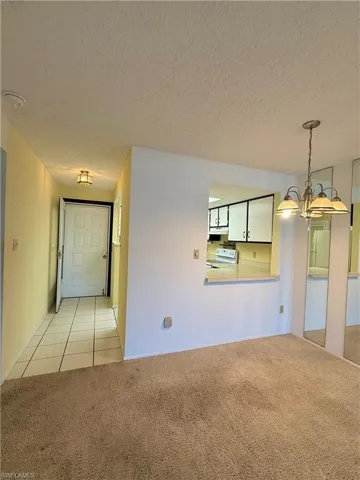 Empty room featuring a textured ceiling, light colored carpet, a chandelier, and light tile patterned floors