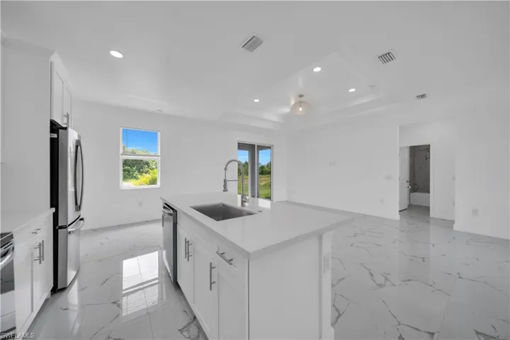 Kitchen with recessed lighting, light marble finish floors, a kitchen island with sink, stainless steel appliances, and light countertops