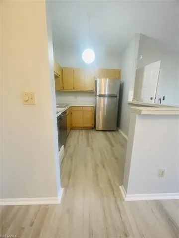 Kitchen featuring freestanding refrigerator, light countertops, hanging light fixtures, and light wood finish cabinets