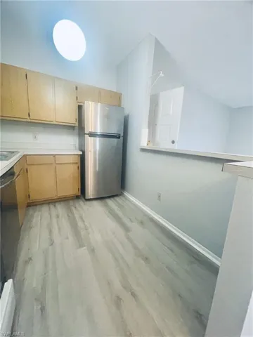 Kitchen featuring light countertops, stainless steel appliances, light wood-style flooring, light wood finish cabinets, and lofted ceiling
