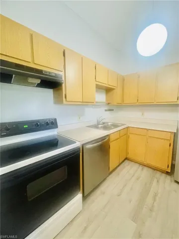 Kitchen featuring electric range oven, light wood finish cabinets, light countertops, light wood-style flooring, and dishwasher