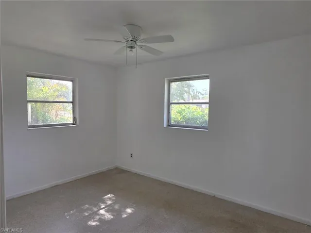 Spacious room featuring neutral carpeting, white walls, and two windows providing outdoor visibility