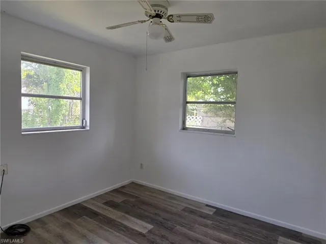 Room featuring wood-finish flooring, two windows, painted walls, and a ceiling fan with integrated lighting