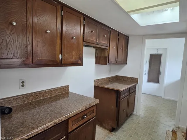 Kitchen featuring wood-finish cabinetry with silver-tone hardware, speckled countertops with a matching backsplash, and a ceiling-mounted skylight