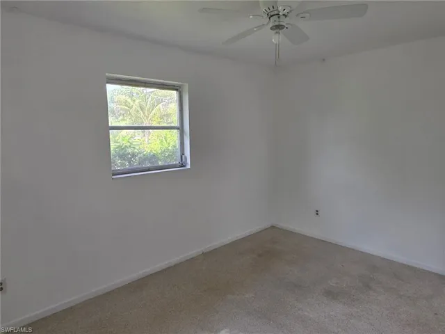 White interior walls with a single window, a ceiling fan with integrated lighting, and carpeted flooring