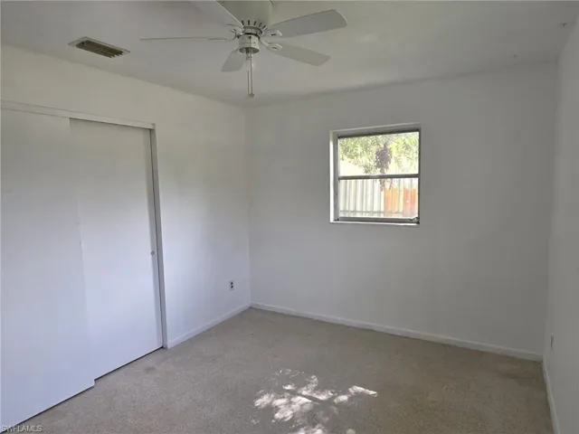 Neutral-toned carpeting paired with white walls, featuring a ceiling fan and a window