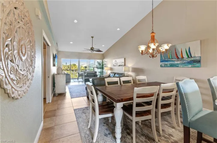 Dining room with tile patterned flooring, ceiling fan with notable chandelier, and high vaulted ceiling