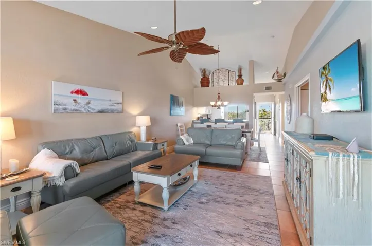 Living room featuring light tile patterned floors, ceiling fan with notable chandelier, and high vaulted ceiling