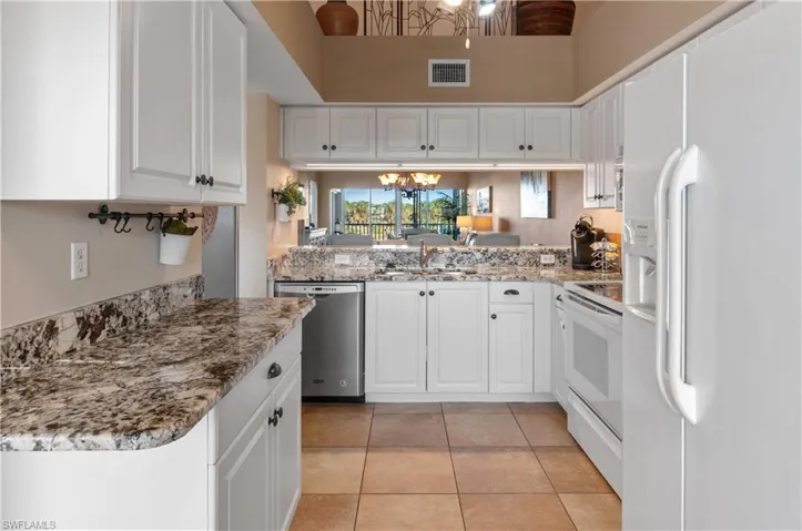 Kitchen with light stone counters, white appliances, sink, light tile patterned floors, and white cabinetry