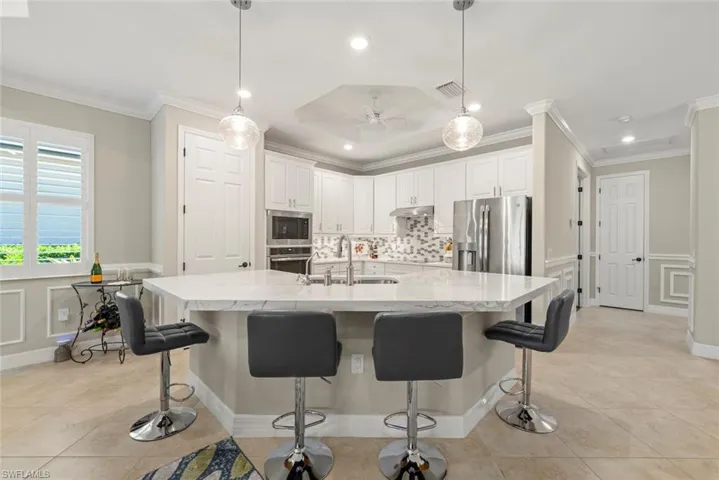 Kitchen featuring a large island with a light-toned quartz countertop, white cabinetry, integrated stainless steel appliances, pendant lighting, pantry and tile flooring