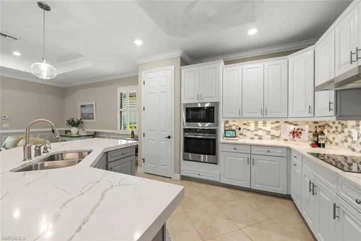 White cabinetry, built-in stainless steel appliances, patterned tile backsplash, pantry, oversized kitchen island with integrated sink, and light-toned tile flooring