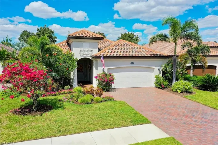 Twin Eagles single family home with two car garage, tiled roof, brick paver driveway, and lush tropical landscaping.